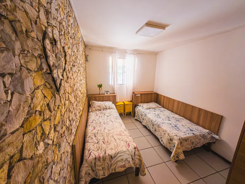 Quarto com duas camas e parede de pedra na unidade Calafate/Prado